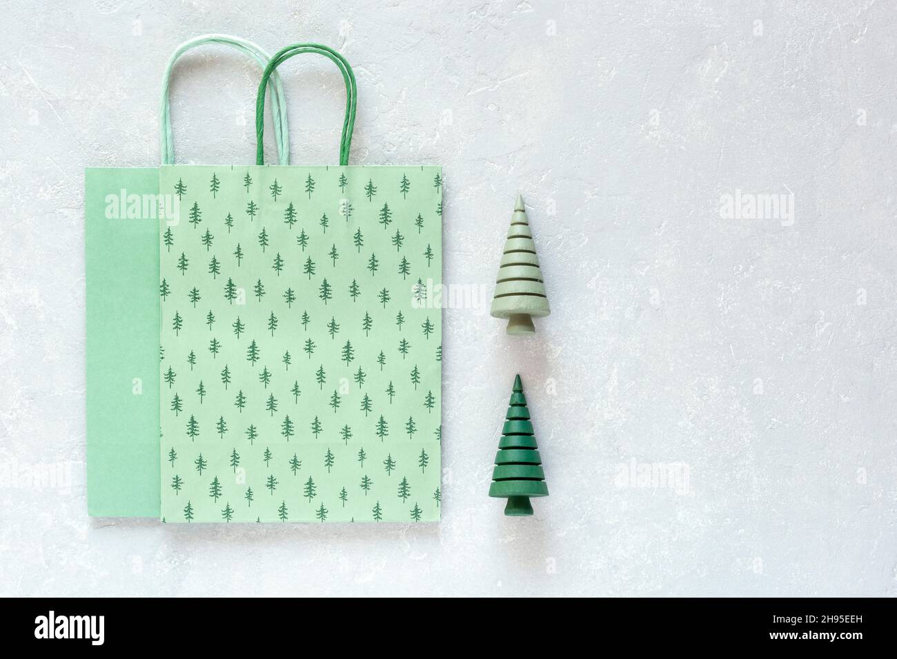 Sacs de Noël en papier vert et arbres de Noël en bois sur fond gris Banque D'Images