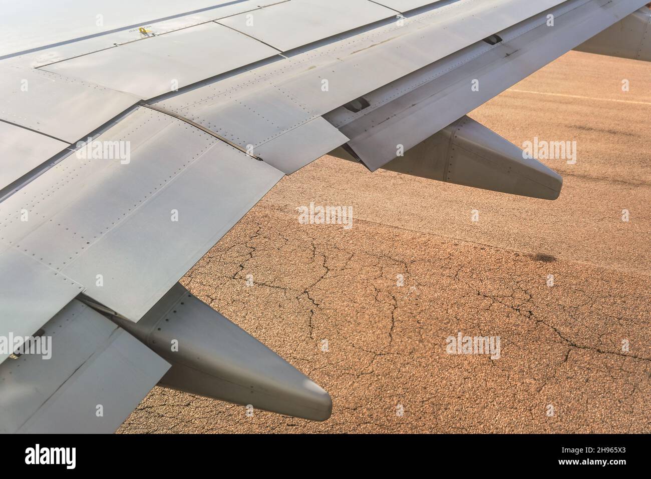 Vue depuis la fenêtre d'un avion commercial, asphalte brun sur la piste visible sous l'aile Banque D'Images