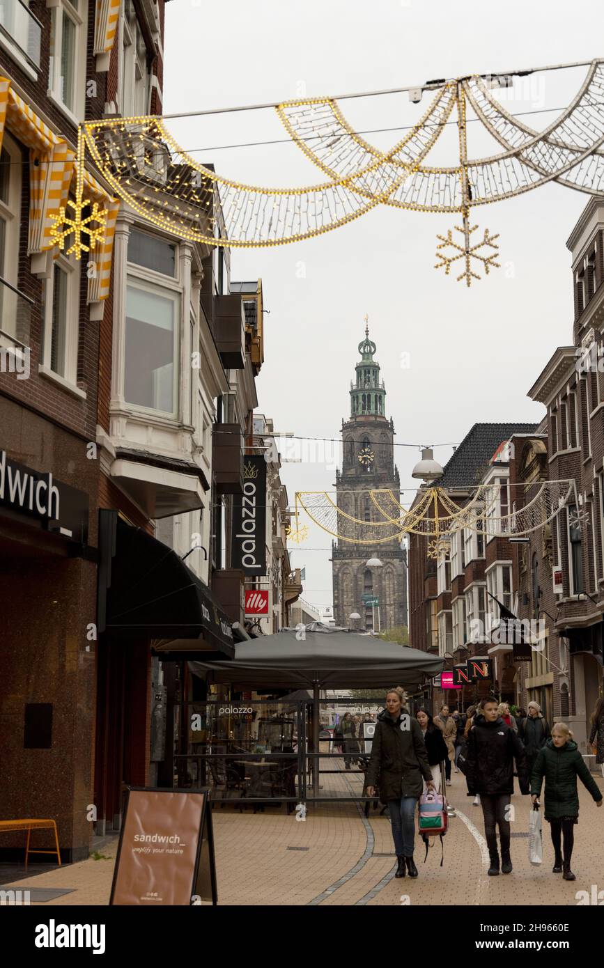 Les gens se promènent sous les lumières et les décorations de Noël sur Zwanestraat en regardant vers le Martinitoren dans la ville de Groningen, pays-Bas. Banque D'Images