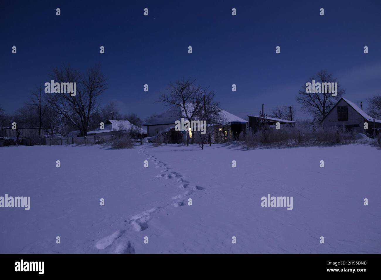 Paysage nocturne d'un champ enneigé.Dans la distance est vu le village.Il y a les empreintes sur la neige. Banque D'Images