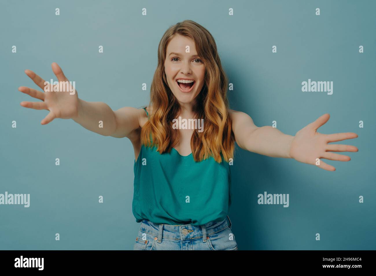 Joyeuse femme excitée répand ses bras larges pour embrasser quelqu'un aimé, isolé sur fond bleu Banque D'Images