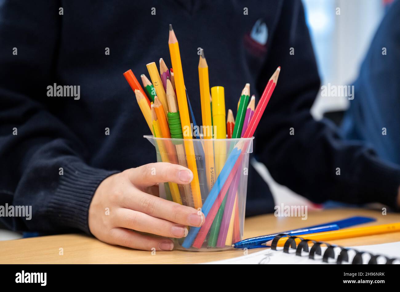 Un enfant tient un pot de crayons dans une école primaire. Banque D'Images