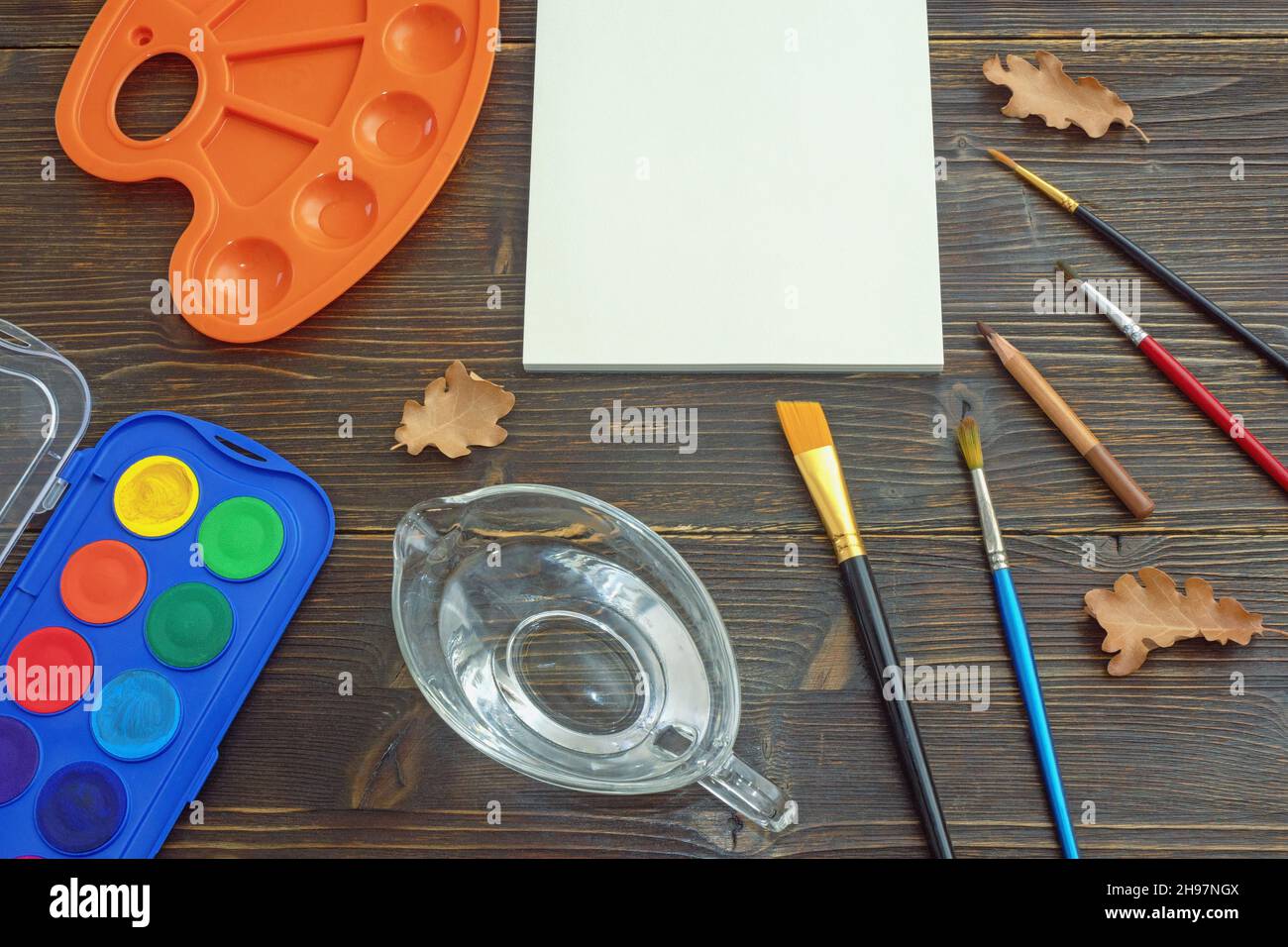 Aquarelle.Ouvrez le carnet d'esquisses, la palette, la tasse d'eau, les pinceaux et le crayon sur une table rustique.Concept scolaire.Espace libre pour le texte ou l'image Banque D'Images