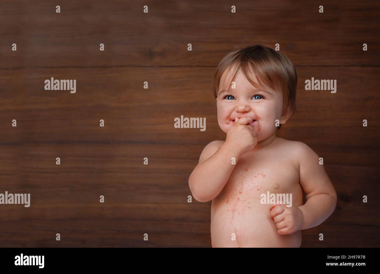 Bébé mange une baie sur fond de bois.L'enfant mange une baie rouge, le jus de la baie a pollué le ventre. Banque D'Images