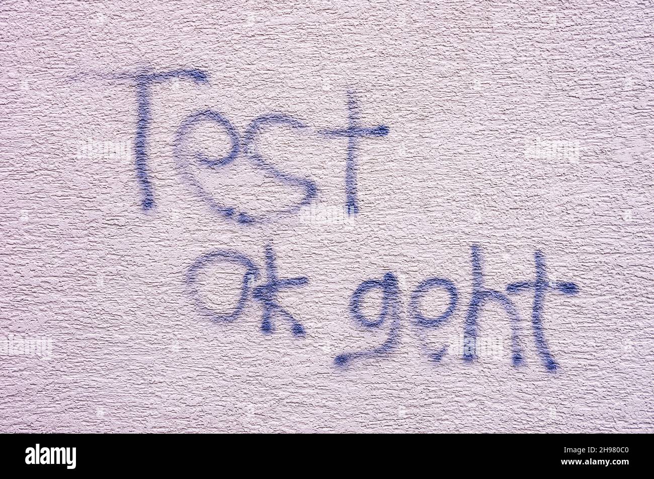 Graffiti avec le texte allemand 'Test ok geht' sur un mur avec plâtre blanc. Banque D'Images