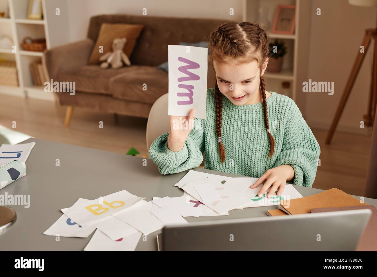 Enfant assis à la table et montrant la carte avec la lettre tout en étudiant en ligne à l'aide d'un ordinateur portable Banque D'Images