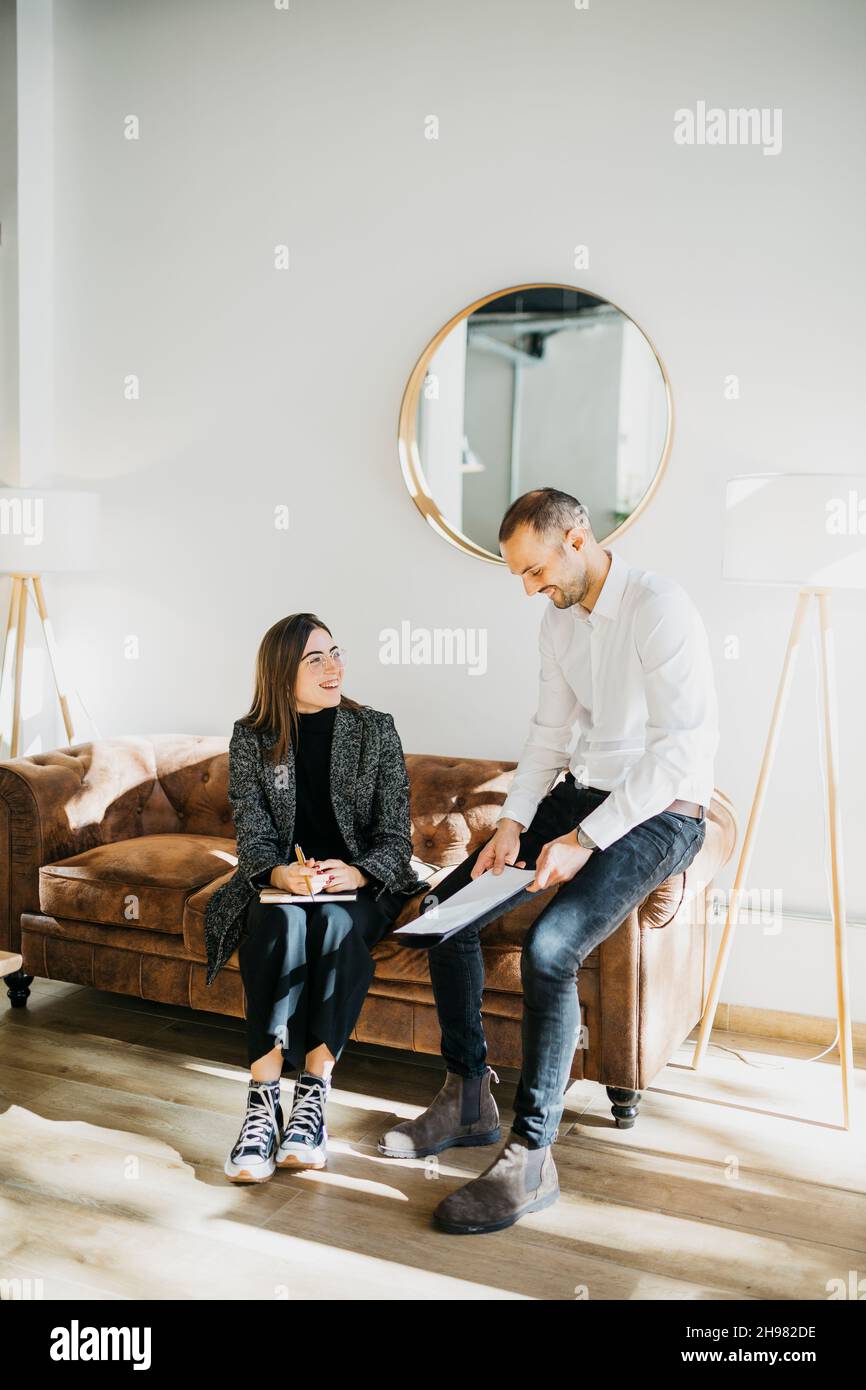 Femme d'affaires et homme d'affaires ayant une conversation informelle, sur un canapé au bureau.Ils sont en mode chic et décontracté. Banque D'Images