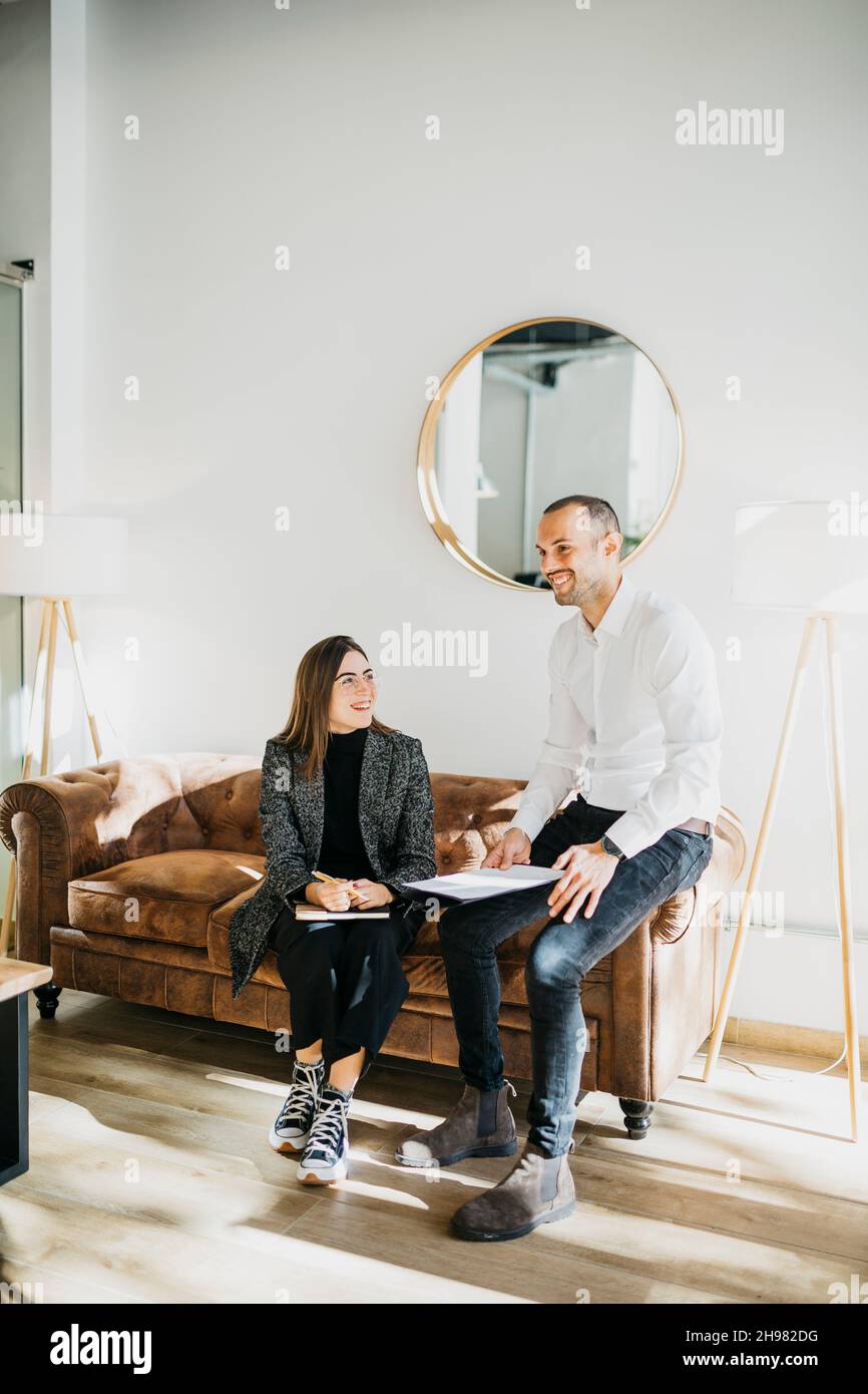 Femme d'affaires et homme d'affaires ayant une conversation informelle, sur un canapé au bureau.Ils sont en mode chic et décontracté. Banque D'Images