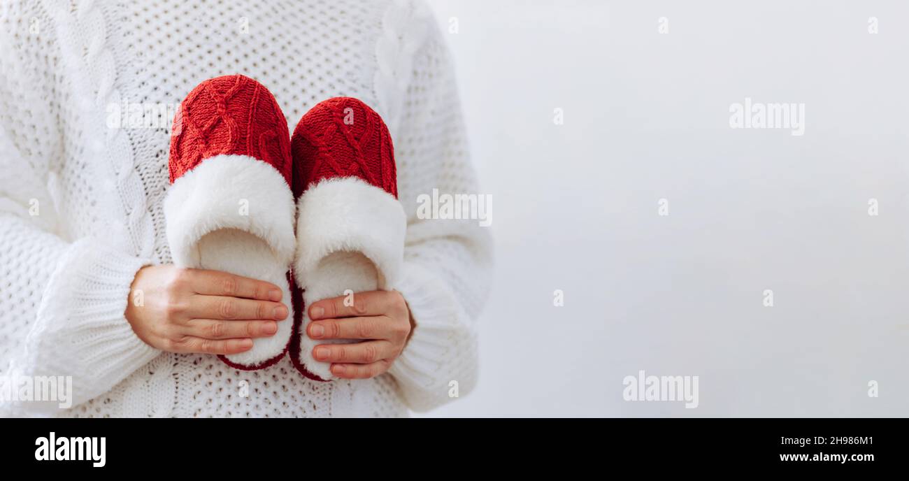 Femme en chandail blanc tient chaud tricoté chaussons rouges.Concept de maison famille vacances confortables Noël nouvel an. Banque D'Images