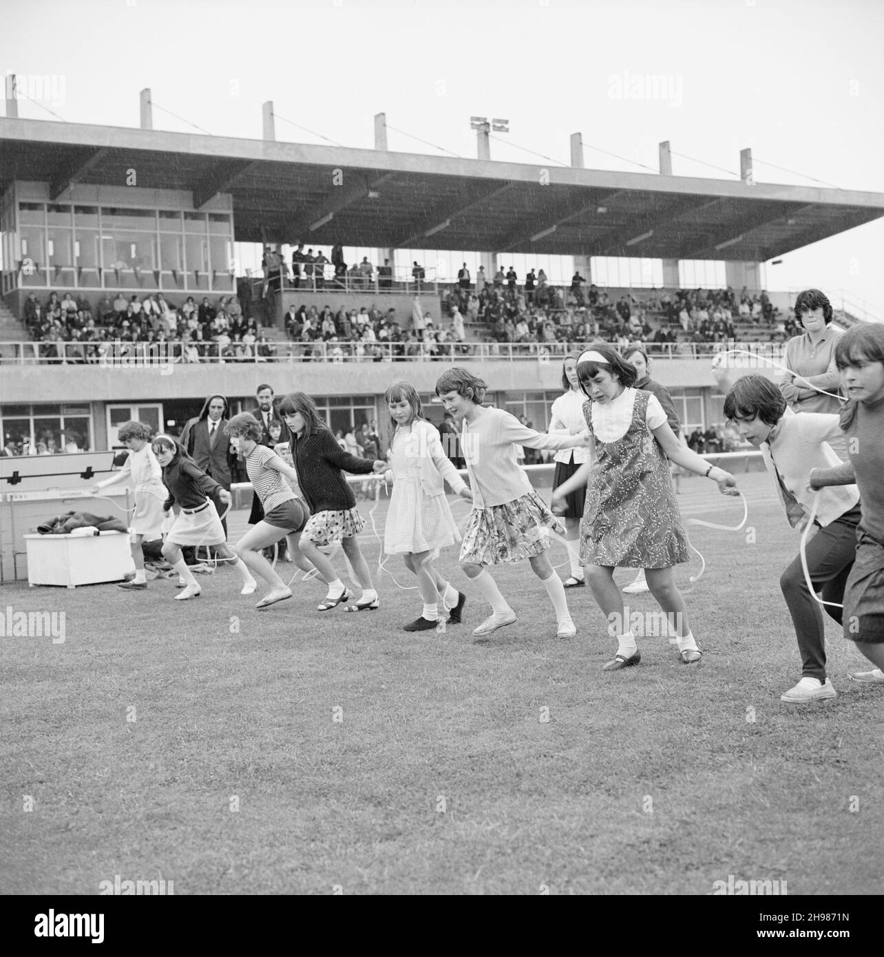 Stade Copthall, Hendon, Barnett, Londres, 25/06/1966.Des filles avec des cordes à sauter alignées au début d'une course à sauter, avec des spectateurs dans un stand au-delà, à la Journée annuelle des sports de Laing qui s'est tenue au stade Copthall.En 1966, la Journée annuelle des sports des employés de Laing a eu lieu le 25 juin au stade Copthall à Hendon.C'était la première fois que l'événement s'y tenait, ayant eu lieu auparavant le terrain de sport de Laing à Elstree.Parmi les différents événements, on compte l'athlétisme et une compétition de football, et les concurrents ont voyagé depuis les bureaux et sites régionaux de la société, notamment en Écosse et en voiture Banque D'Images