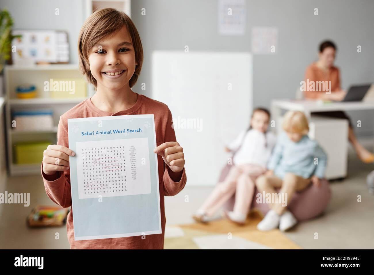 Portrait d'un enfant heureux souriant à l'appareil photo tout en montrant son papier avec l'exercice en anglais debout dans la salle de classe Banque D'Images