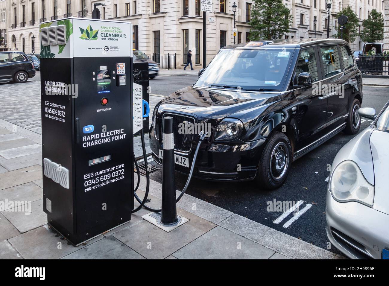 Une cabine électrique noire TX (fabriquée par LEVC) se recharge à un point de charge électrique rapide à St James's Square, Londres SW1, Royaume-Uni Banque D'Images