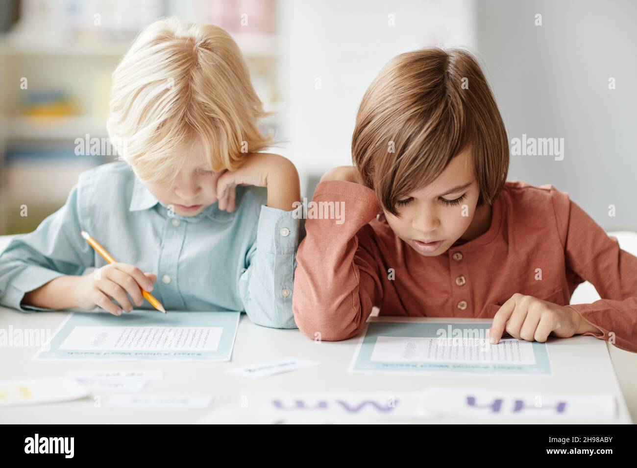 Les écoliers qui font des notes sur le papier tout en étant assis à la table pendant la leçon Banque D'Images