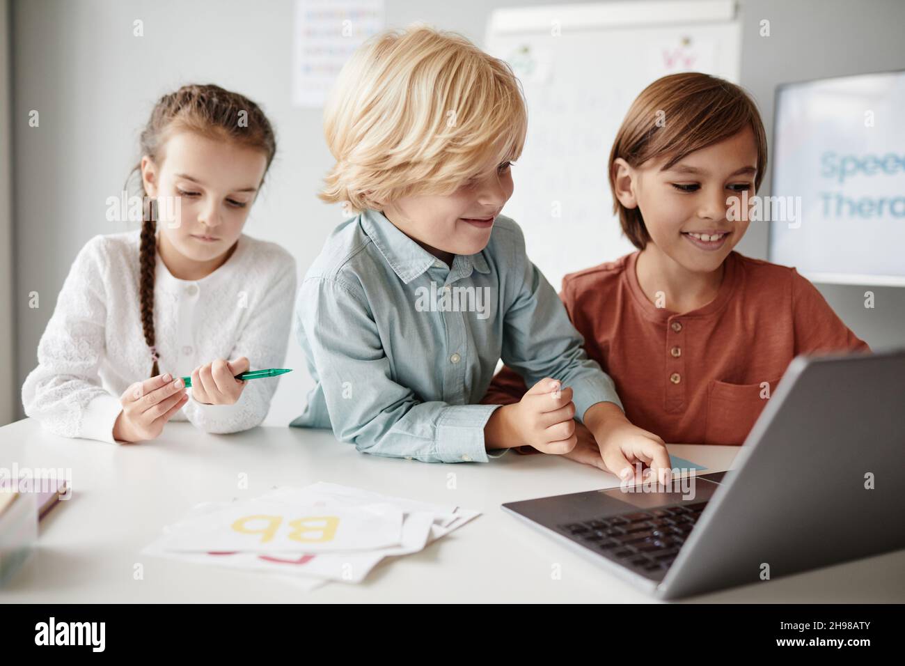 Groupe d'enfants assis à la table et dactylographiant sur ordinateur portable pendant une leçon, ils étudient en ligne Banque D'Images