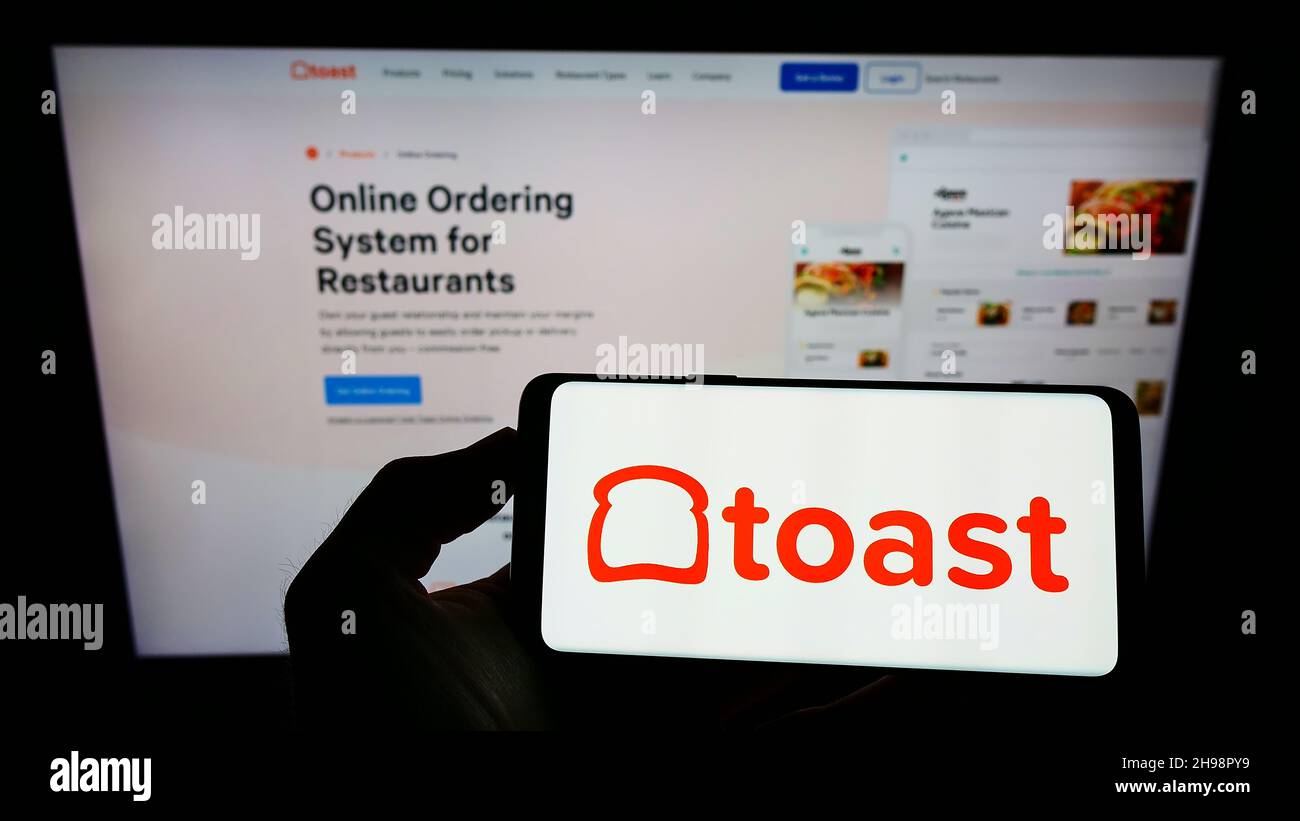 Personne tenant un smartphone avec le logo de la société américaine de logiciel de restaurant Toast Inc. À l'écran devant le site Web.Mise au point sur l'affichage du téléphone. Banque D'Images