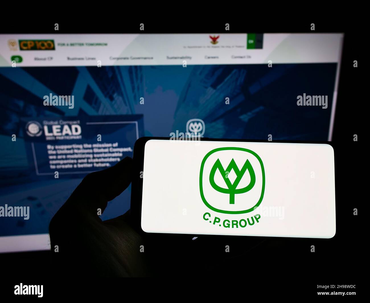 Personne tenant un téléphone portable avec le logo du conglomérat thaïlandais Chaloen Pokphand Group (CP) à l'écran en face de la page web.Mise au point sur l'affichage du téléphone. Banque D'Images