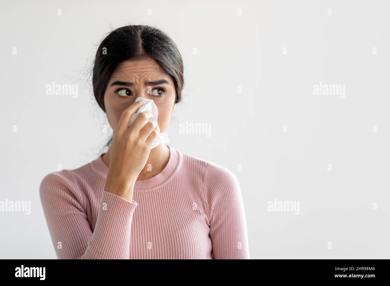 Une jeune femme indienne sérieuse éternue dans une serviette et souffle son nez sur un fond de mur gris Banque D'Images