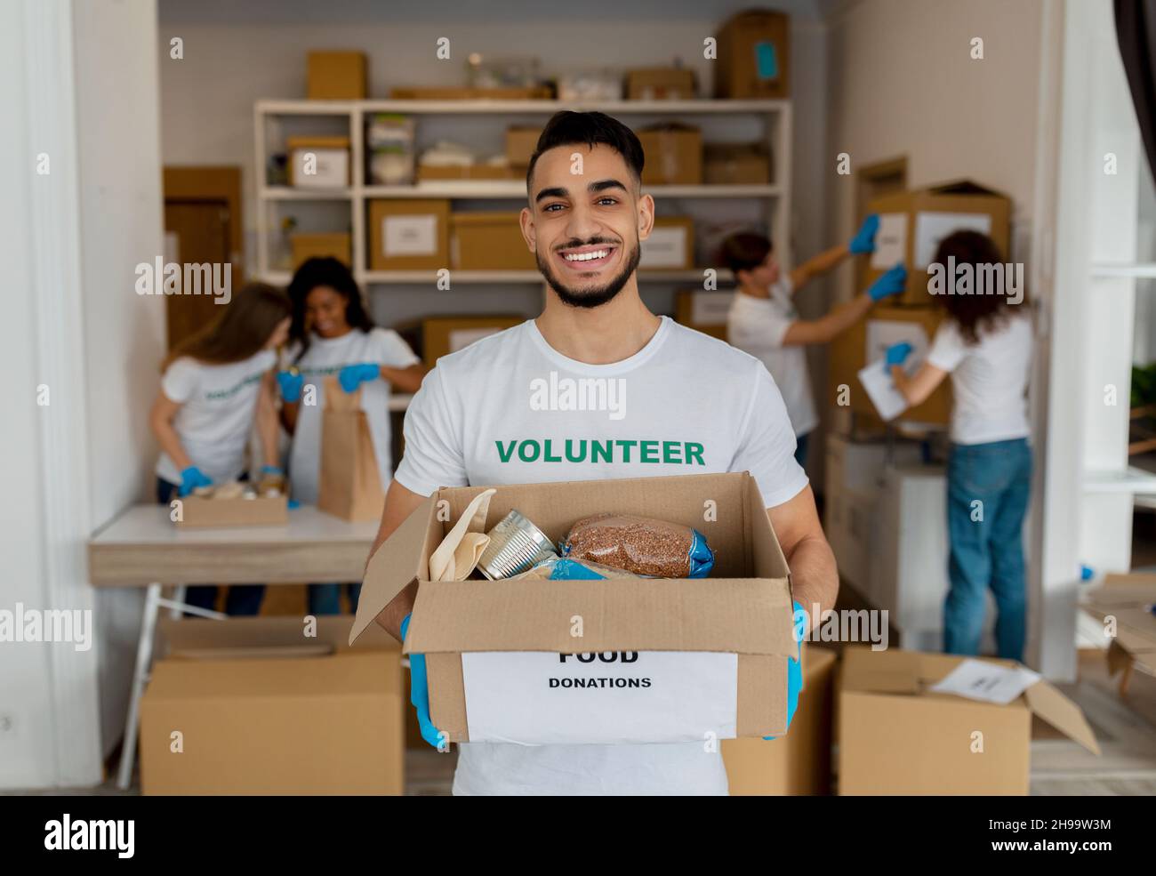 Aide humanitaire.Un volontaire arabe masculin tient une boîte en carton avec des produits, travaillant avec des collègues au centre de charité Banque D'Images