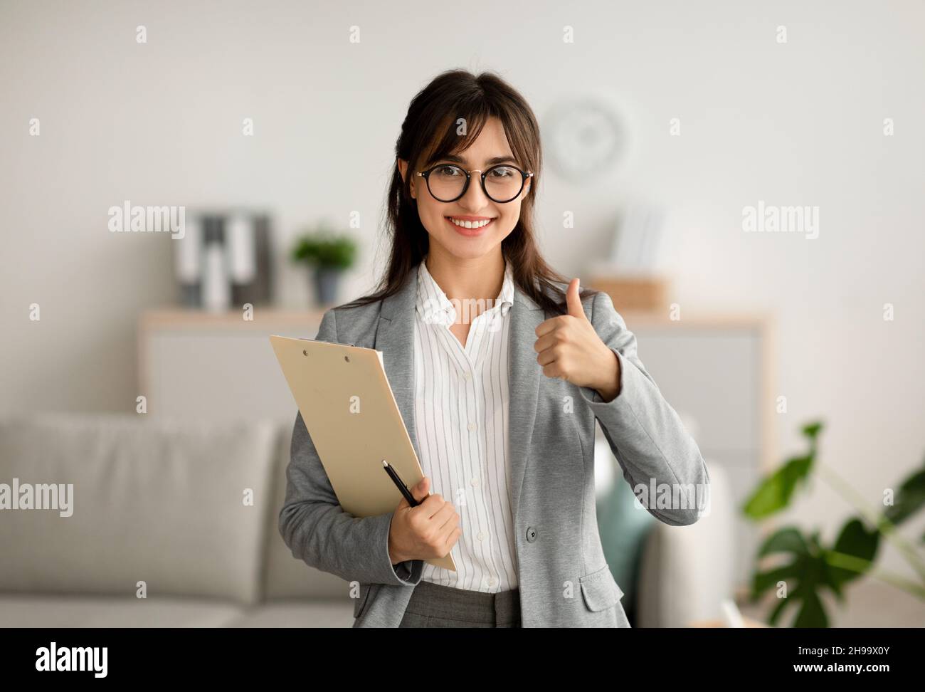 Jeune professionnelle psychologue gestante pouce vers le haut signe travaillant dans le bureau et souriant à la caméra, espace libre Banque D'Images