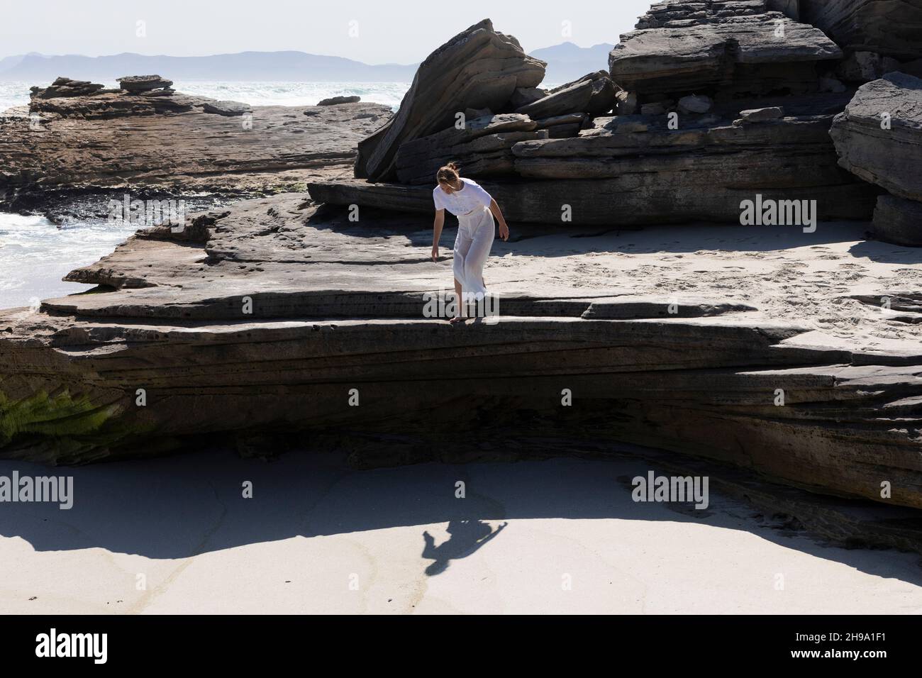 Une adolescente se prépare à sauter de rochers lisses et plats au-dessus d'une plage de sable Banque D'Images