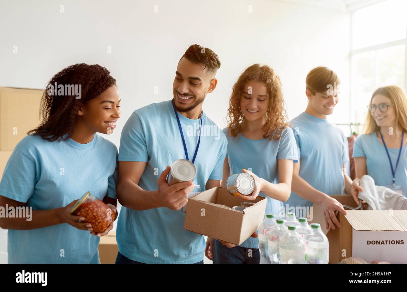 Concept d'aide humanitaire.De jeunes bénévoles divers trient et emballant des conserves dans des boîtes en carton, travaillant ensemble Banque D'Images