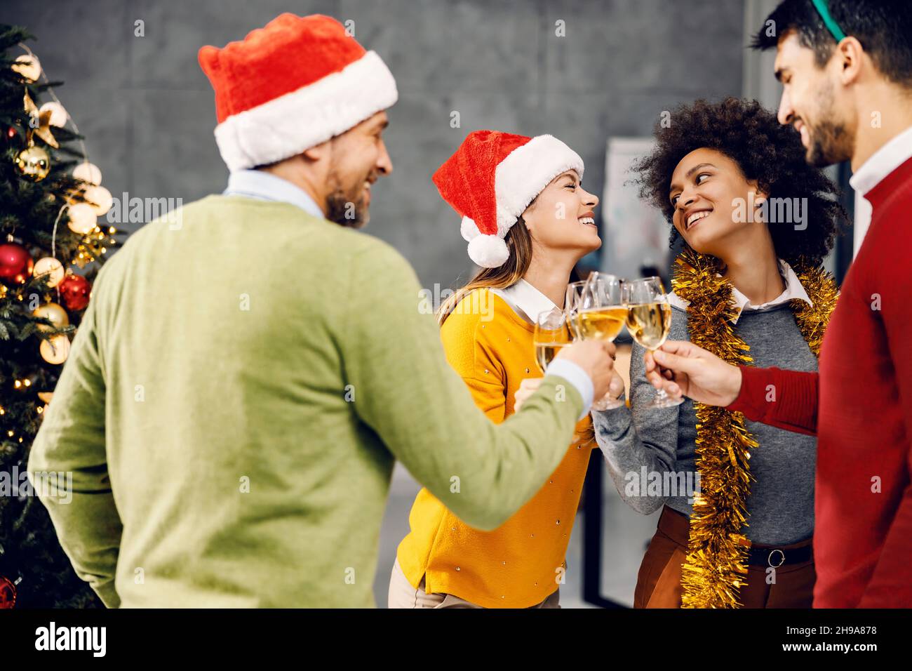Célébration du nouvel an dans une entreprise.Un groupe de collègues multiraciaux se tenant à côté d'un arbre de Noël et faisant un toast avec des verres de cha Banque D'Images