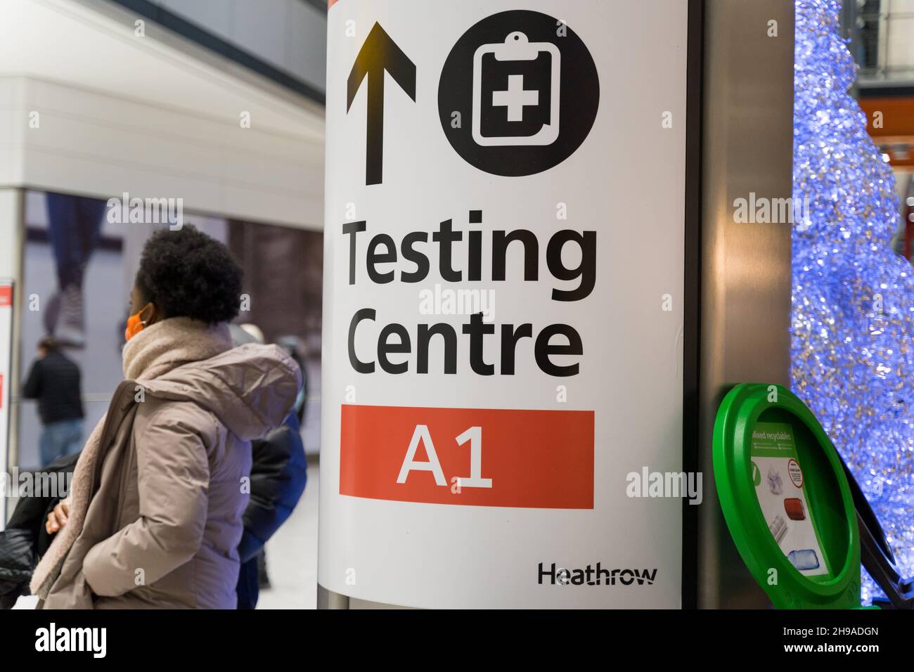 Une femme voyageur se trouve à côté de l'affiche pour le centre d'essais Covid-19 au terminal de l'aéroport de Londres Heathrow, Angleterre, Royaume-Uni Banque D'Images