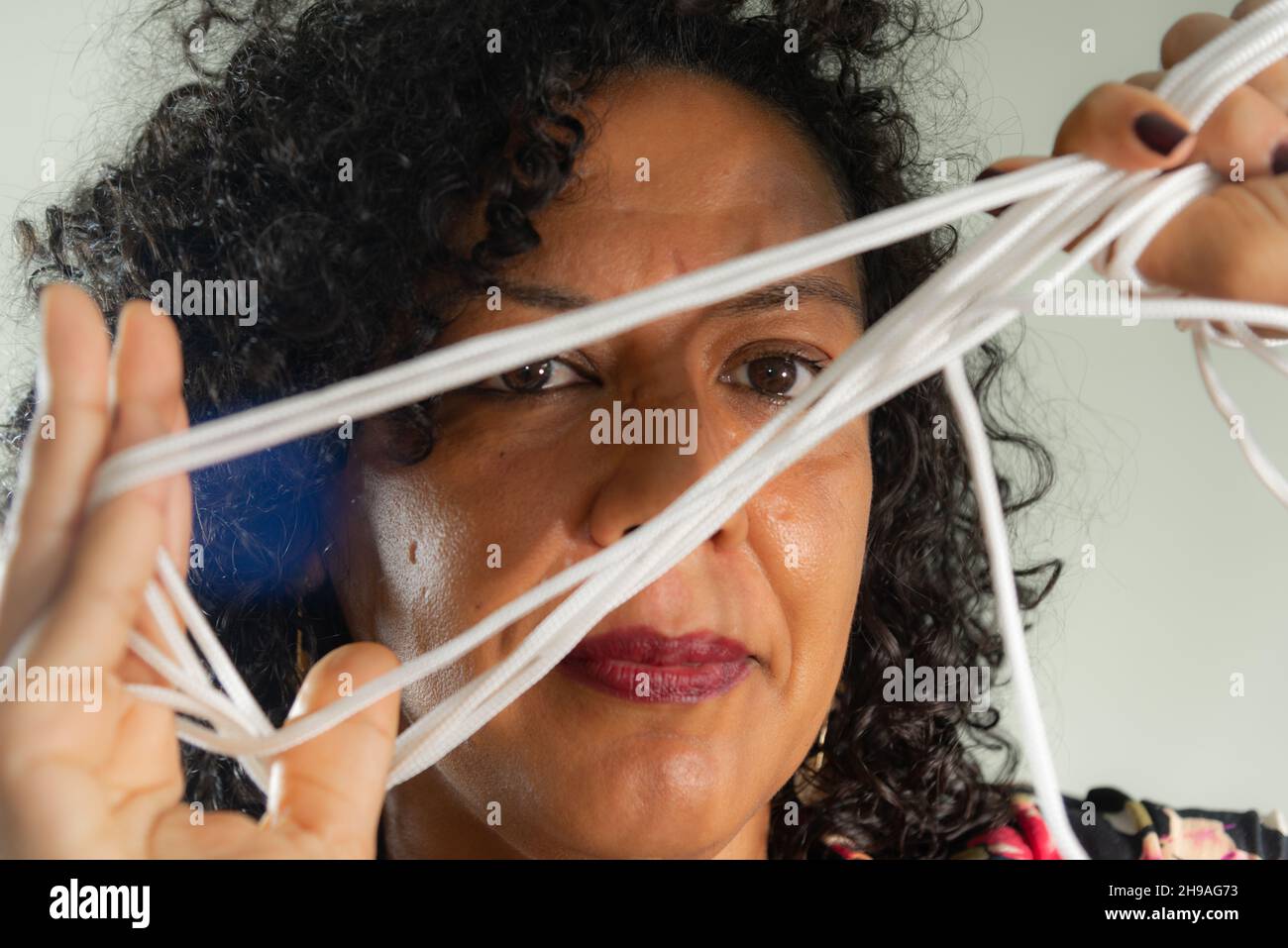 Gros plan du visage d'une femme portant une robe colorée avec cordon dans les mains sur fond gris clair.Salvador, Bahia, Brésil. Banque D'Images