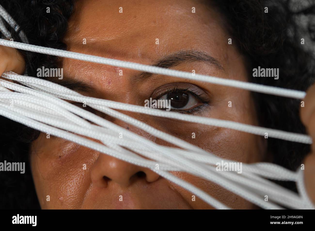 Gros plan du visage d'une femme portant une robe colorée avec cordon dans les mains sur fond gris clair.Salvador, Bahia, Brésil. Banque D'Images