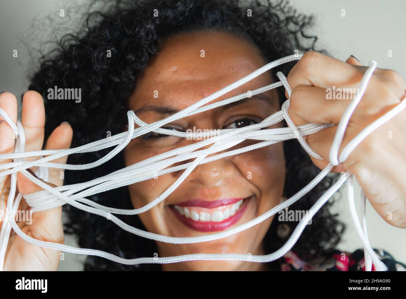 Gros plan du visage d'une femme portant une robe colorée avec cordon dans les mains sur fond gris clair.Salvador, Bahia, Brésil. Banque D'Images