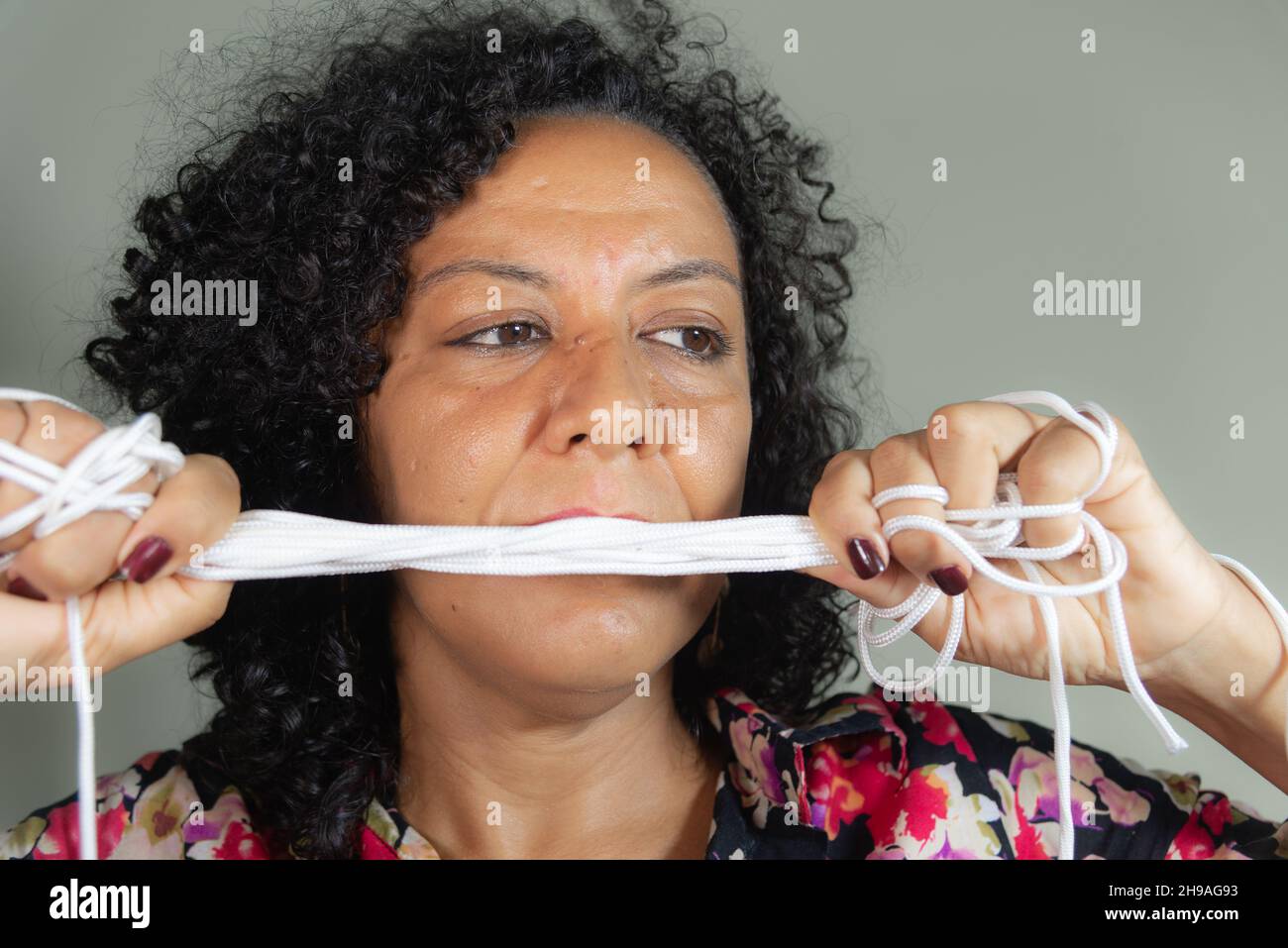 Gros plan du visage d'une femme portant une robe colorée avec cordon dans les mains sur fond gris clair.Salvador, Bahia, Brésil. Banque D'Images