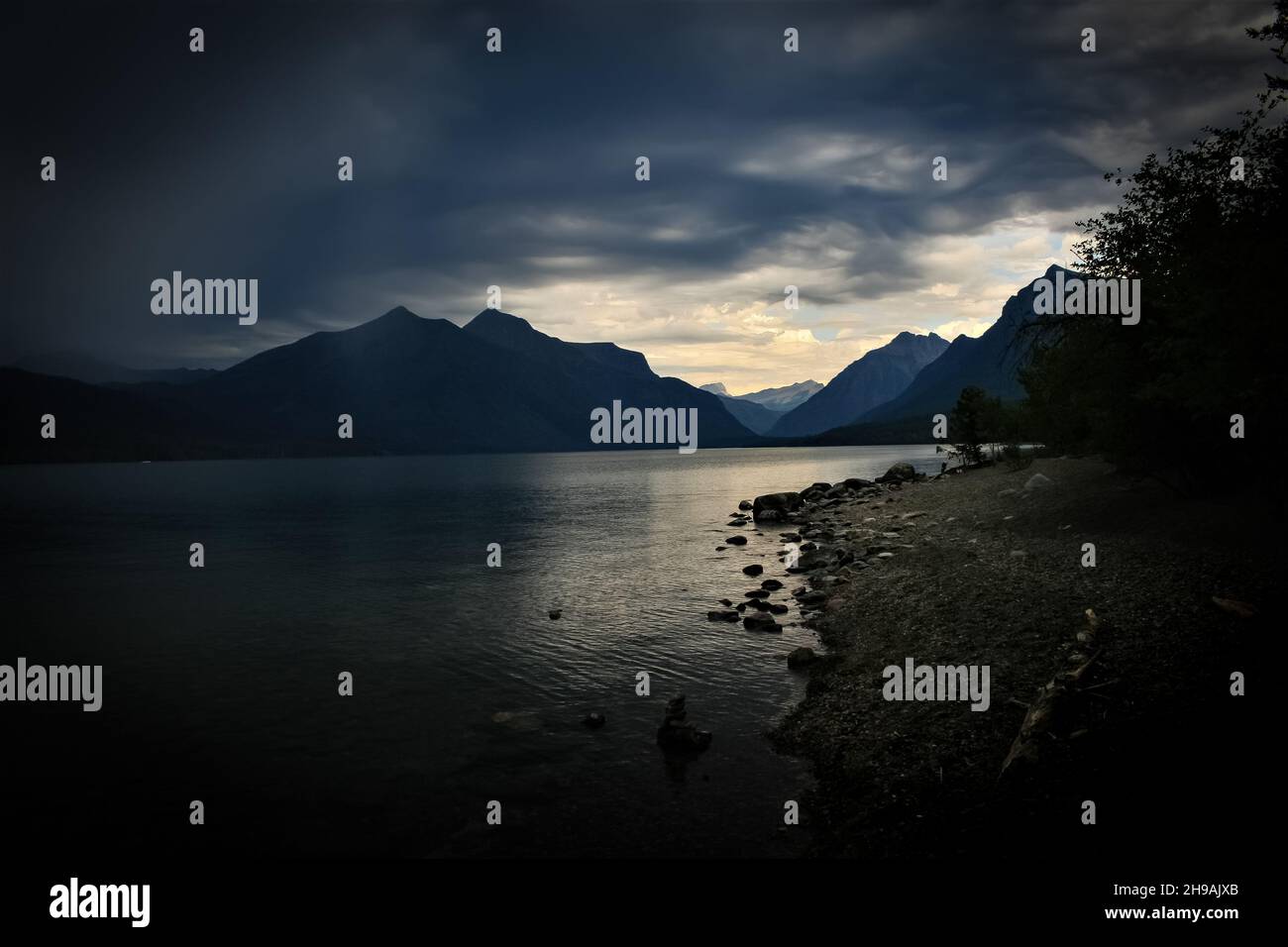 Rive du lac de montagne bordée par la forêt avec la pluie empiétant causant des ombres profondes Banque D'Images