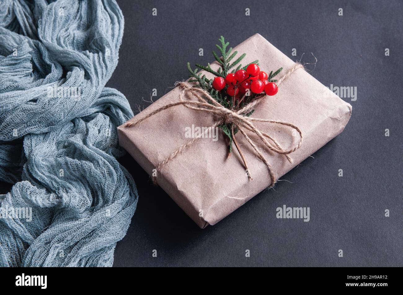 Boîte cadeau à côté de la nappe vintage grise et laisse des baies rouges sur une table en bois marron Banque D'Images