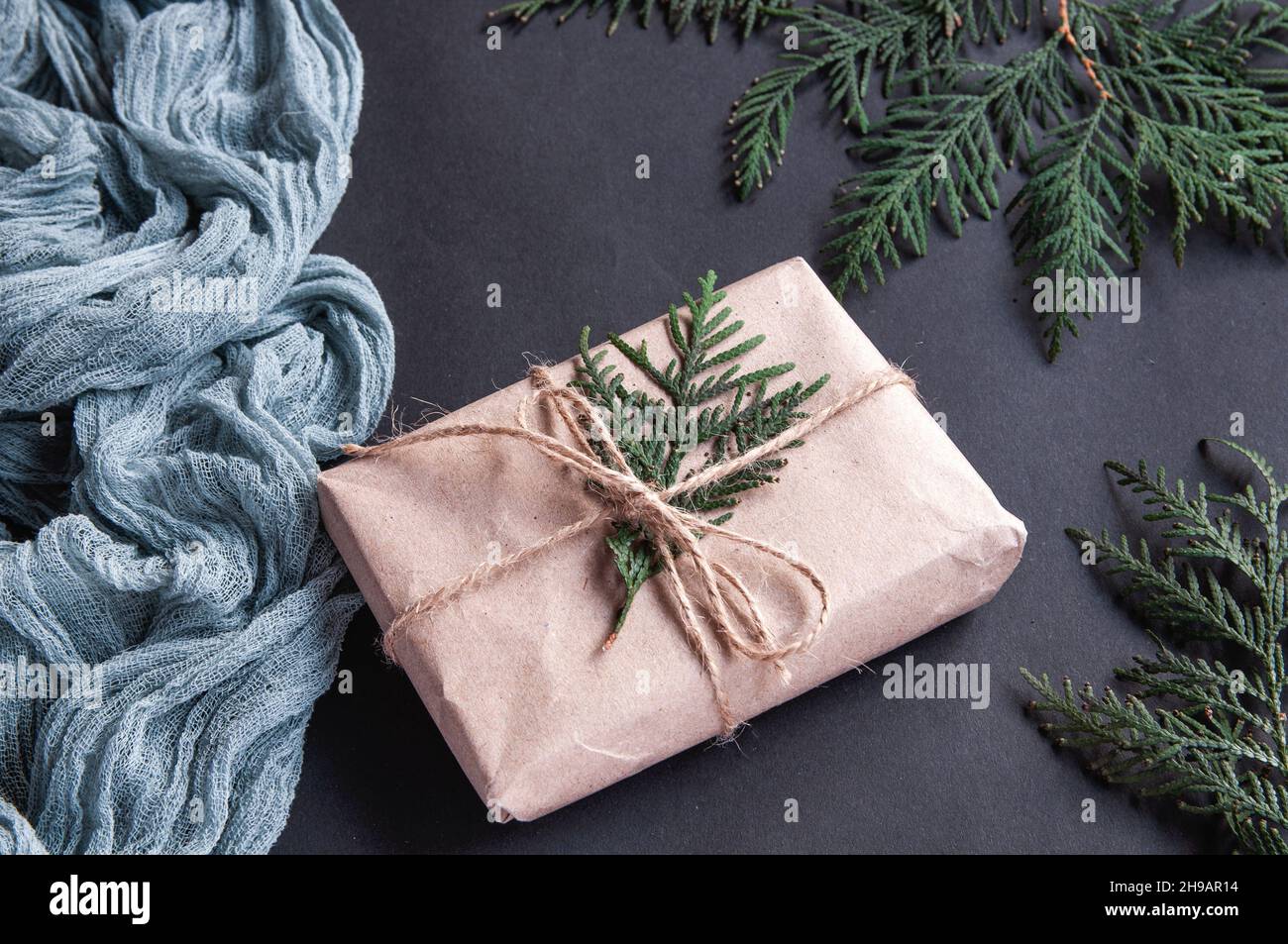 Boîte-cadeau à côté de la nappe rétro grise et feuilles d'épinette avec baies rouges sur fond noir Banque D'Images