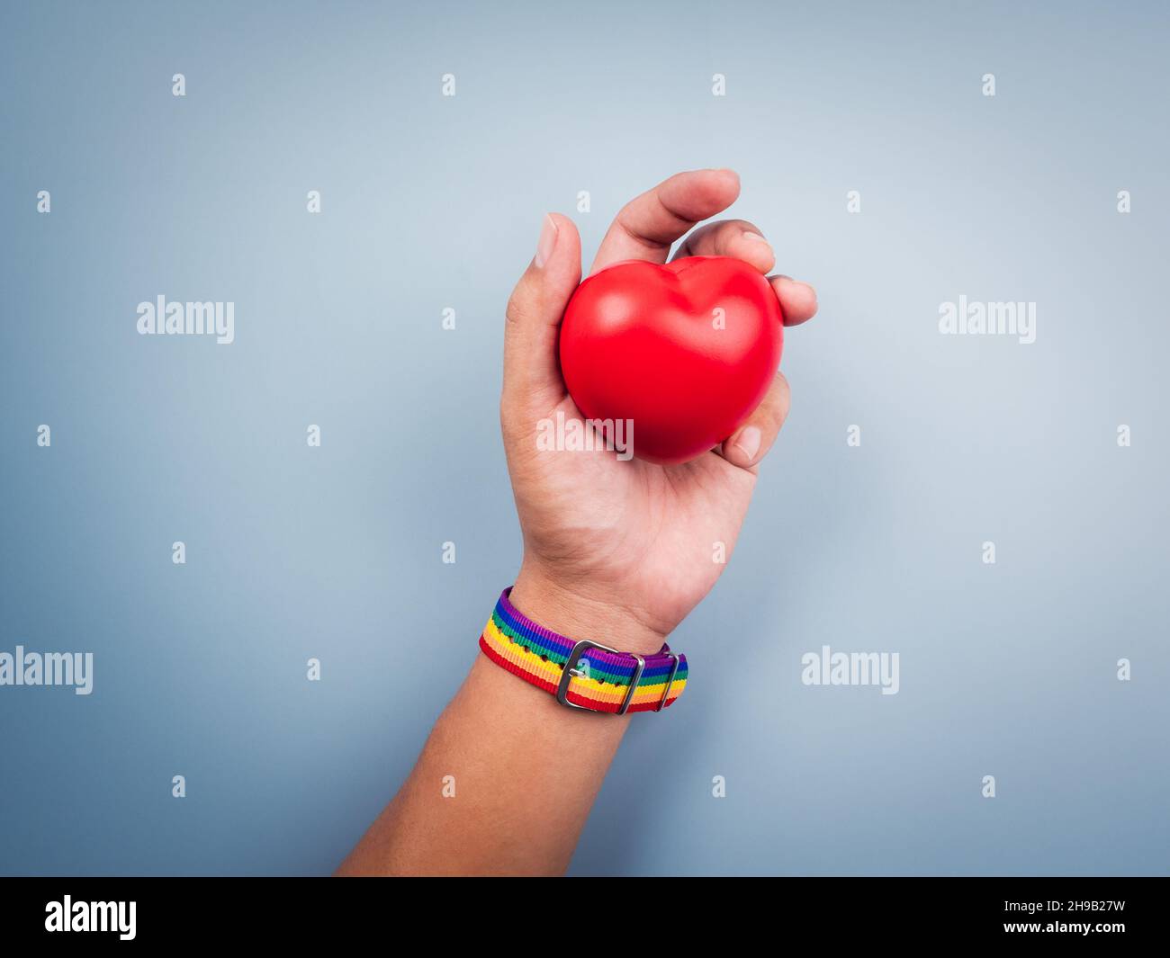 Main avec une petite ceinture de drapeau arc-en-ciel tenant et montrant une balle de coeur rouge sur fond bleu.Le concept LGBT avec couleurs de fierté et bande de drapeau arc-en-ciel. Banque D'Images