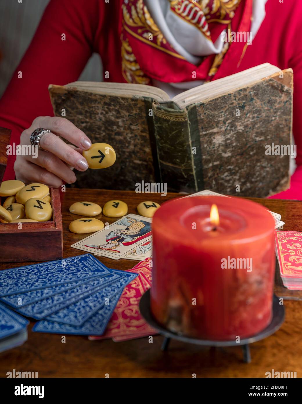 Un caissier de fortune habillé en rouge lit des cartes et un livre ancien pour prédire l'avenir Banque D'Images