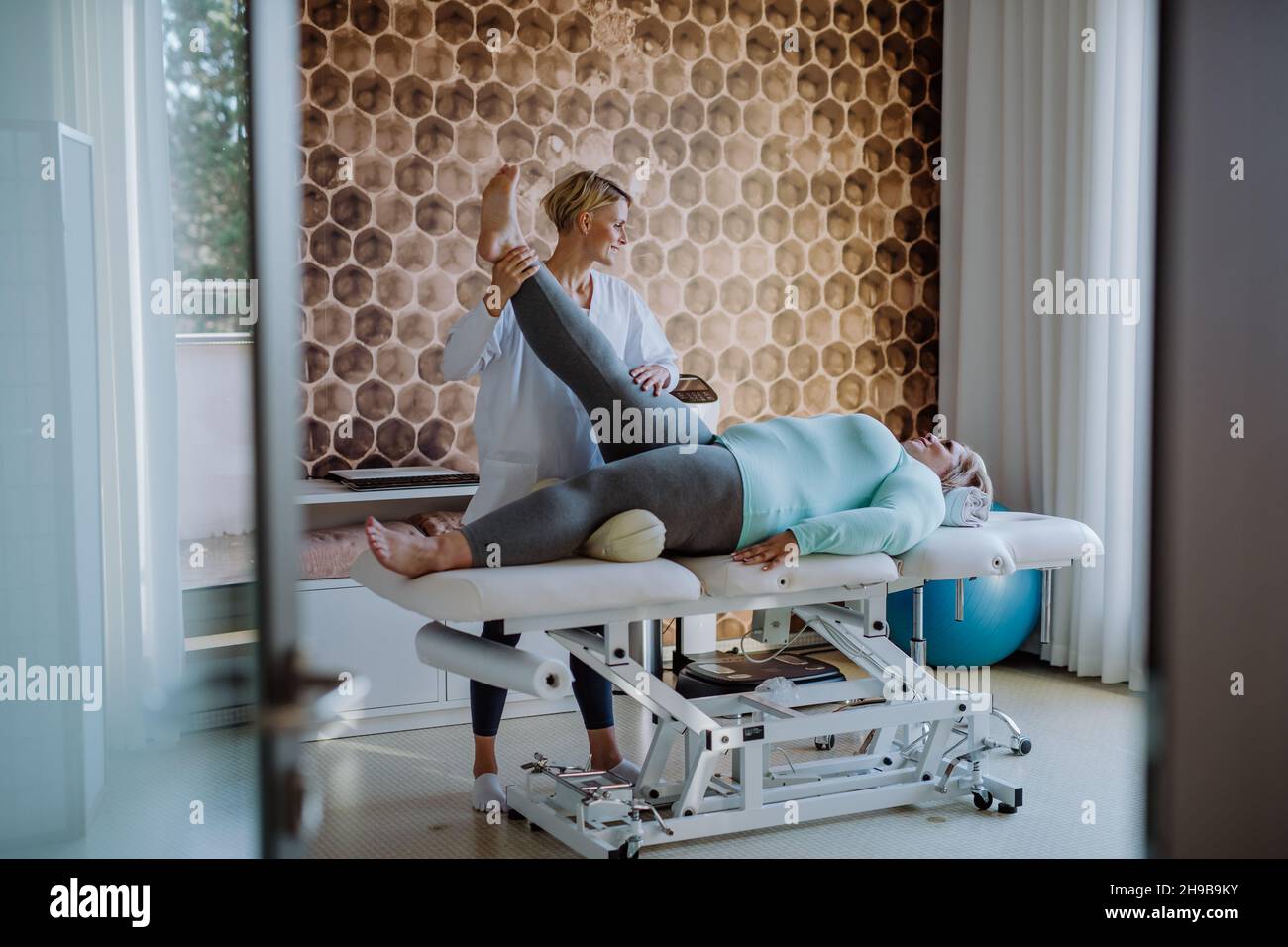 Femme physiothérapeute adulte de taille moyenne s'exerçant avec une femme en surpoids à l'intérieur dans un centre de réadaptation Banque D'Images