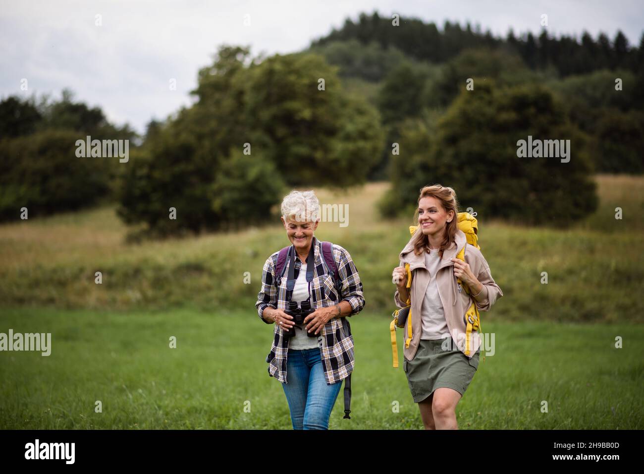 Femme âgée active avec des jumelles en randonnée avec sa fille adulte à l'extérieur dans la nature. Banque D'Images