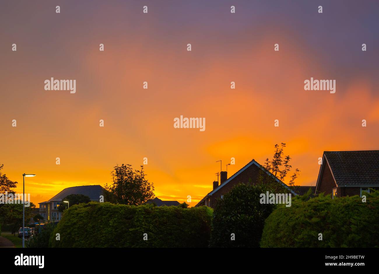 Ciel orange nuageux au-dessus des maisons résidentielles à ou juste après le coucher du soleil en automne à West Sussex, Angleterre, Royaume-Uni. Banque D'Images