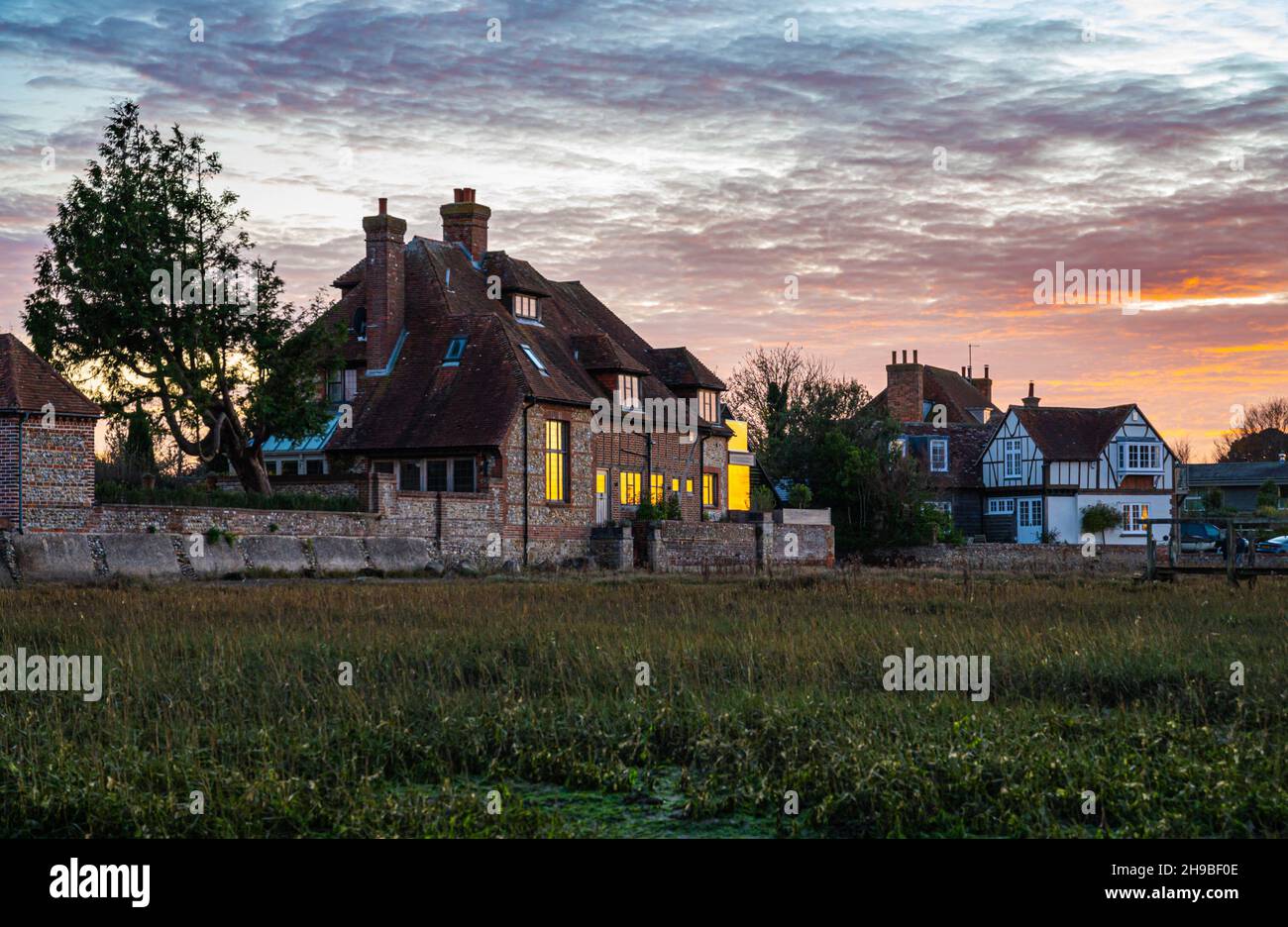 Grandes maisons individuelles en bord de mer à marée basse et en soirée lumière autour du côté lointain de Bosham Quay / Harbour, Bosham Village, West Sussex, Royaume-Uni. Banque D'Images
