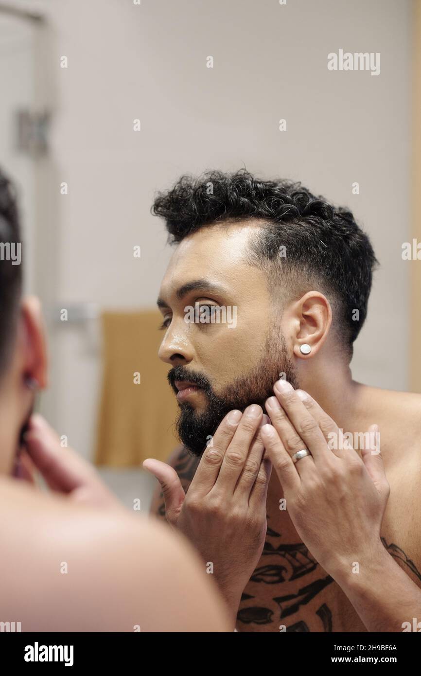 Homme inquiet regardant le miroir et vérifiant à quel point sa barbe est-elle dense après avoir pris la douche Banque D'Images