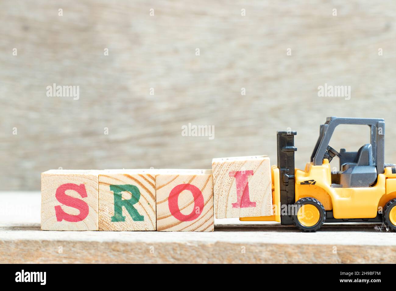 Chariot élévateur à jouets tenir le bloc de lettres I pour compléter le mot SROI (abréviation du retour sur investissement social) sur fond de bois Banque D'Images