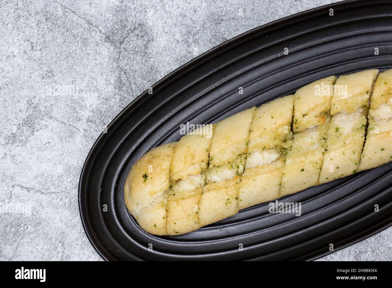 Baguette à pain à l'ail et aux herbes sur une assiette en granit noir.Sur un fond concret Banque D'Images