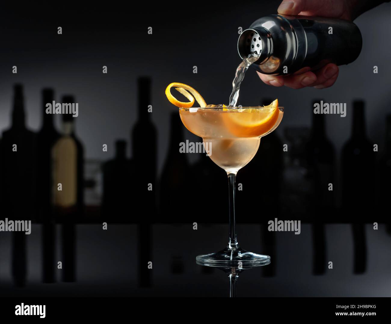 Le barman verse un cocktail d'un shaker dans un verre avec de la glace. Banque D'Images