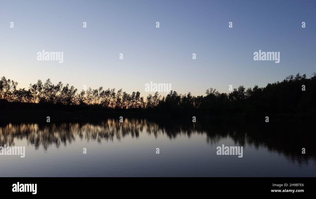 Vue sur un étang juste après le coucher du soleil, dans un parc anglais.Les réflexions des arbres peuvent être vues dans l'eau. Banque D'Images