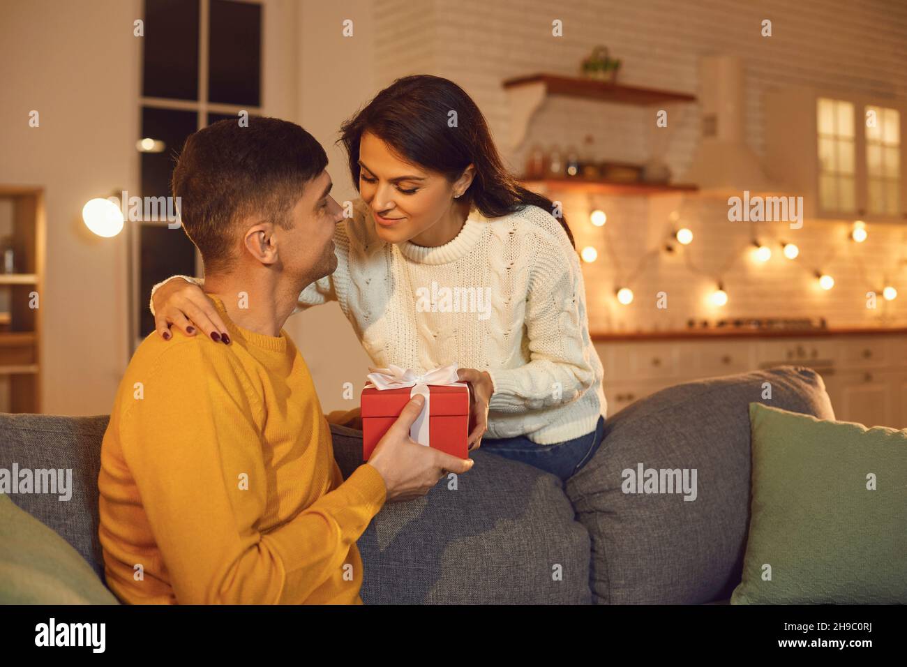Jeune couple heureux en amour assis sur un canapé et donnant des cadeaux de vacances pendant la Saint Valentin Banque D'Images