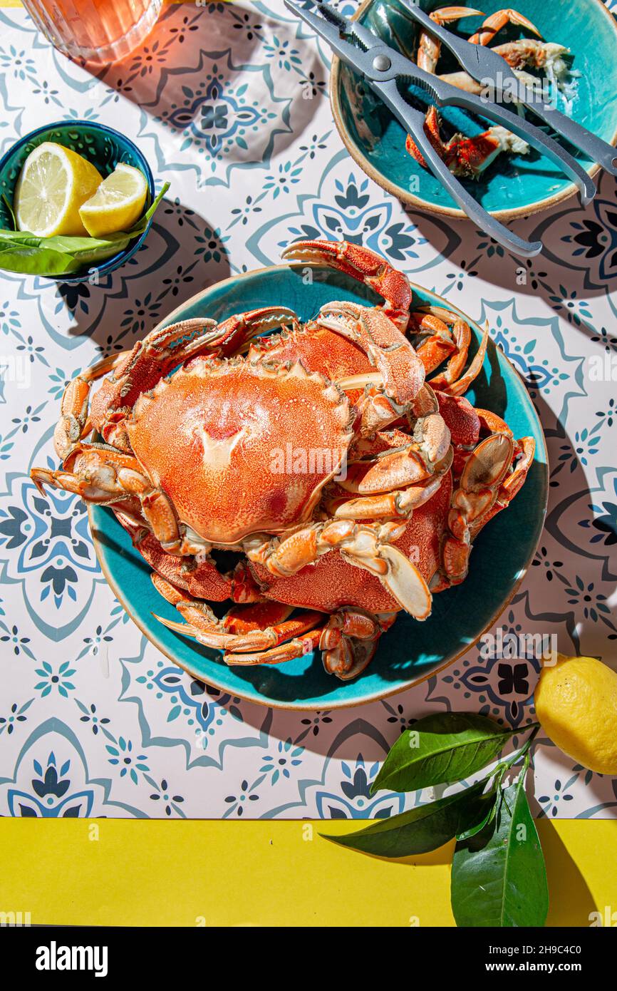 Crabe cuit sur une assiette bleue, citrons, vin de rose sur une table, intensité de lumière du soleil. Banque D'Images