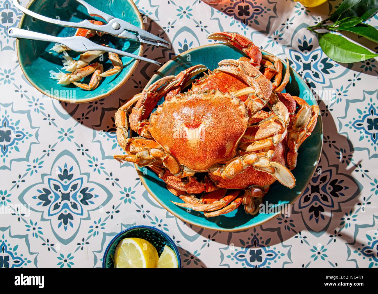 Crabe cuit sur une assiette bleue, citrons, vin de rose sur une table, intensité de lumière du soleil. Banque D'Images