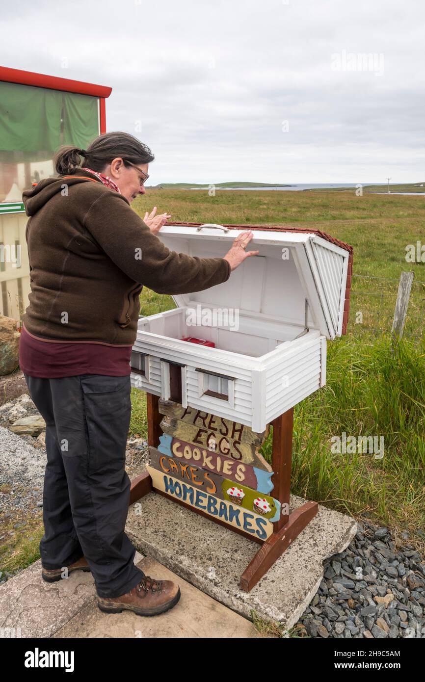 Femme achetant de la nourriture sur un stand de bord de route avec une boîte d'honnêteté à Baltasound sur l'île d'Unst, Shetland. Banque D'Images