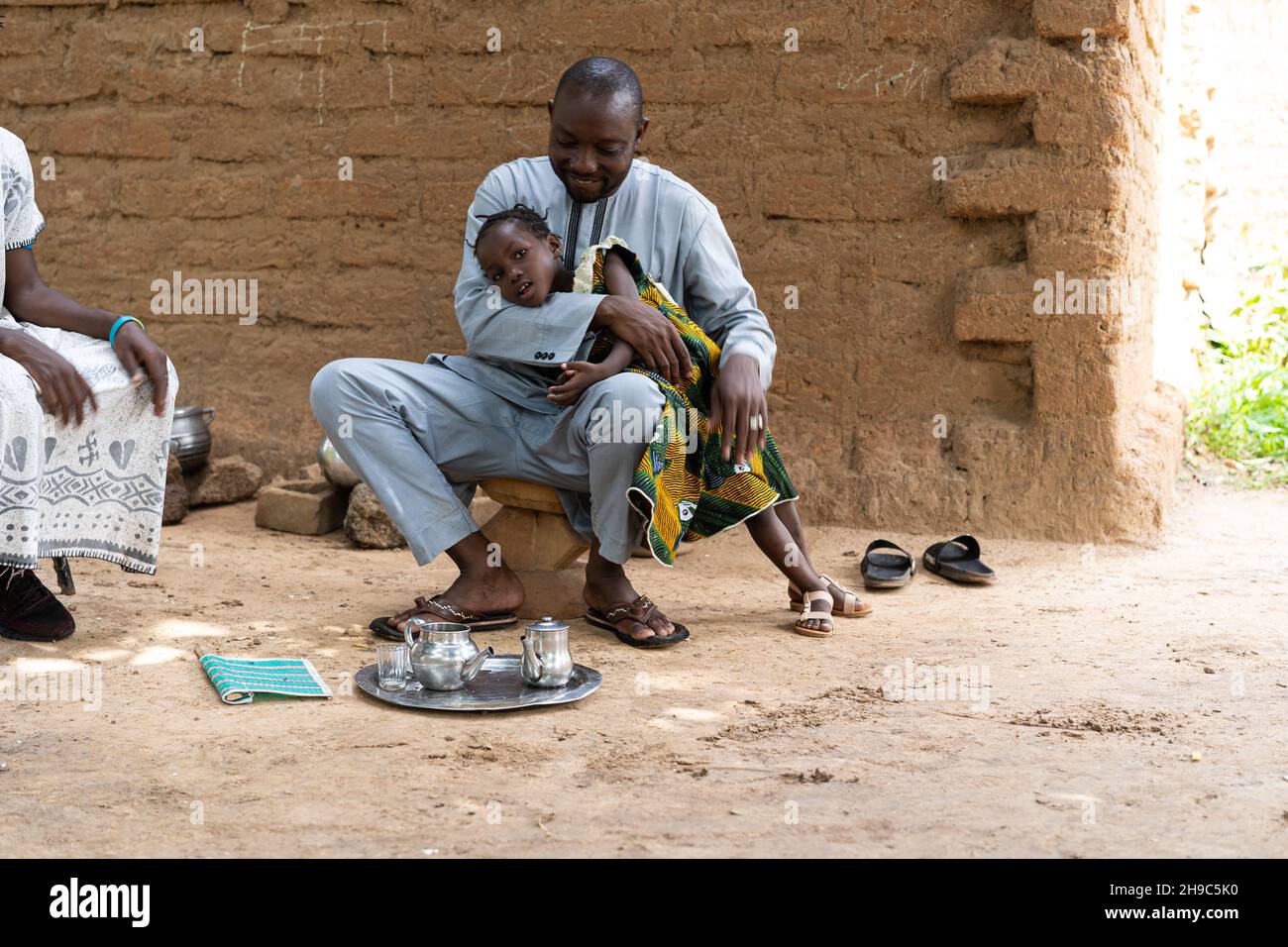 Père noir aimant jouant avec sa fille dans la cour de sa maison de boue traditionnelle en Afrique de l'Ouest Banque D'Images